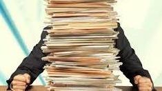 A person hidden behind a tall stack of paperwork on a desk